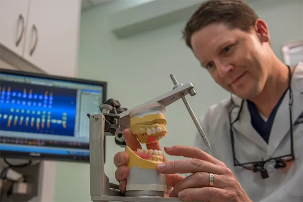 Dr. Cunningham working on the model of a teeth with teeth picture in background.