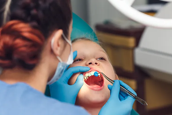 Young boy patiently keeping his mouth open while his female dental assistant does the check up.