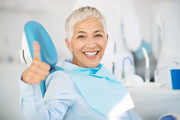 A person showing thumbs up and smiling in a dental chair.