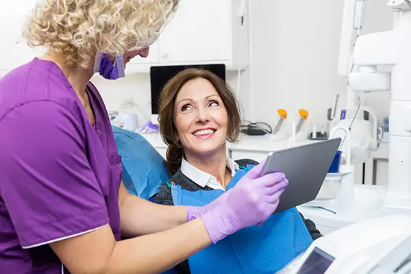 A smiling female patient interacting with her dentist, who is holding a tablet to explain her dental examination results.